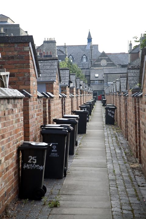 A back alley in Swindon, England, with cobbled paving and several rubbish bins