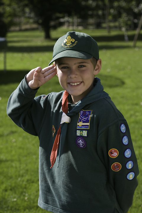 Boy wearing cub scout uniform, saluting, smiling, portrait