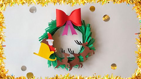 A Christmas wreath with card cut-outs of Santa, his sleigh and three reindeer decorating it.