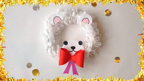 A Christmas wreath of a polar bear head, made from crepe paper. The ears, face and bow are made from card and are stuck onto the wreath.