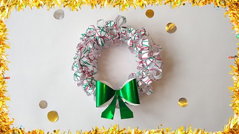 A Christmas wreath made from paper with squiggly felt tip scribbles all over it. It has a big green bow.