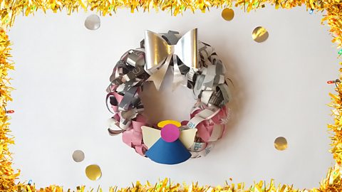 A Christmas wreath made from newspaper, with an angel and a silver bow decorating it.