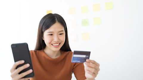 A woman holding a phone and a credit card, smiling.