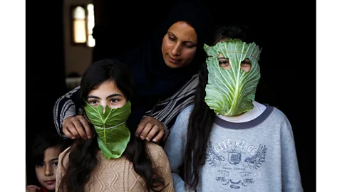 Mohammed Abed/AFP via Getty Images A Palestinian mother entertains her children with makeshift masks made of cabbage as she cooks in Beit Lahia in April 2020 (Credit: Mohammed Abed/AFP via Getty Images)