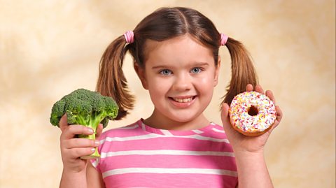 A girl holding up some broccoli and a donut