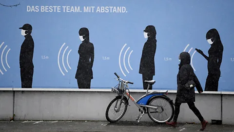 Andreas Gebert/Reuters A woman walks next to a poster in Germany reading "The best team. With distance" (Credit: Andreas Gebert/Reuters)