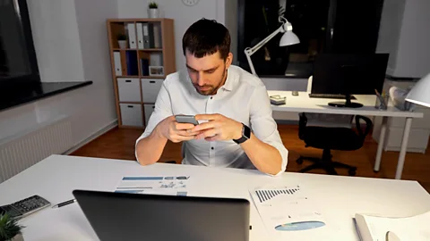 Alamy File image of a man looking at his phone in front of his laptop