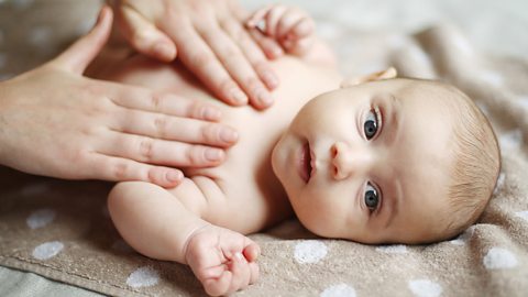 A small baby lies on a towel while a parent gently massages their chest.