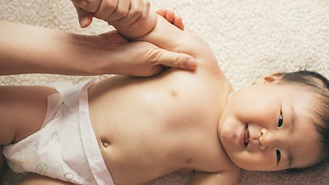 A young baby smiles whilst a parent massages their right arm and shoulder.