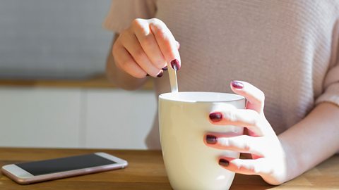 Teen making a cup of tea. There is a phone on the table.