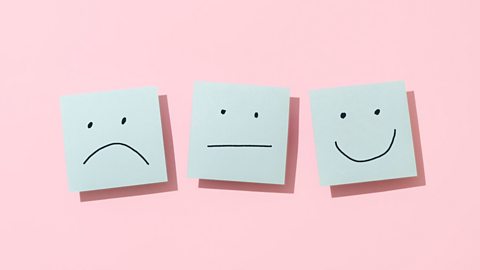 Post-it notes of a sad face; a neutral face; a happy face on a pink background.