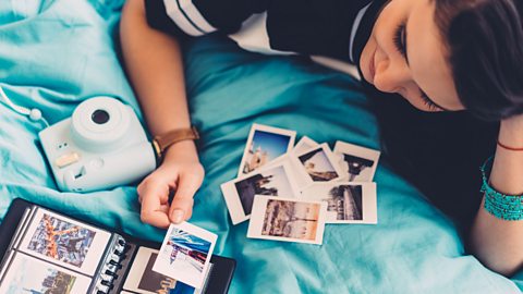 A teen girl on a blue bed looking at polaroid pictures.