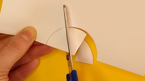 Scissors cutting out a semi-circle on folded paper in sections