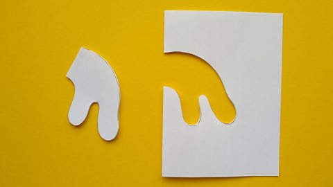 An organic, curvy hole cut out of folded paper, with the shape that was removed