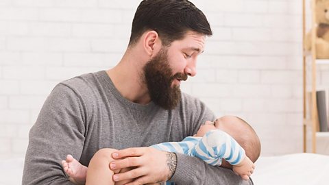 A dad holding a crying baby, looking a bit unsure.