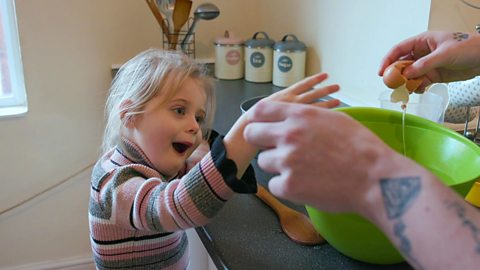 A little girl watching her mum crack an egg.