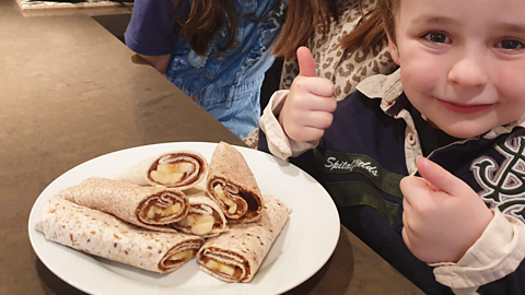 A little boy giving thumbs up to the banana and nut butter wraps.