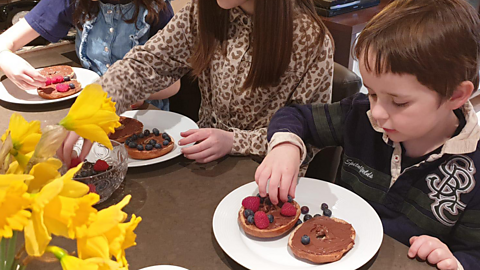 A little boy arranging fruit on a bagel.