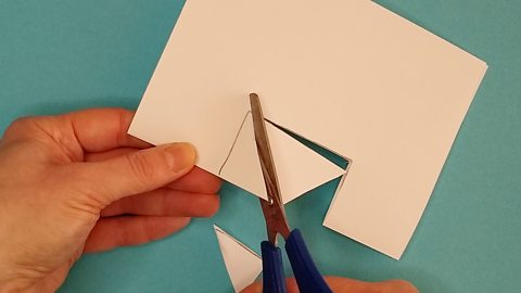 Scissors cut a segment out of a square hole on a piece of paper