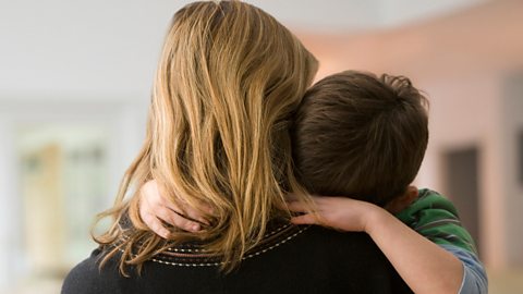 Young boy clings to his mum's shoulder