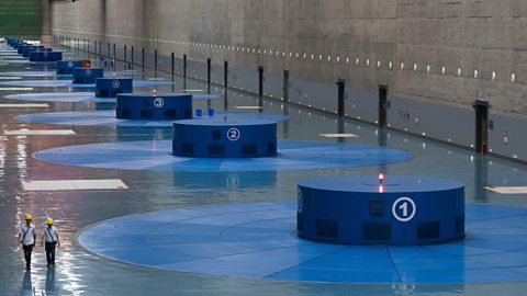 Inside a hydropower station showing a row of generators and two workers