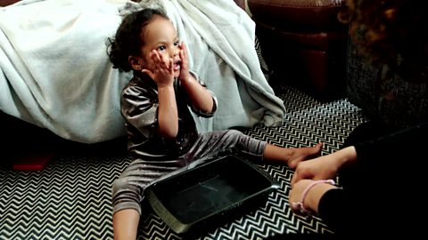 A little girl plays with a tray of water, she's patting it on her face.