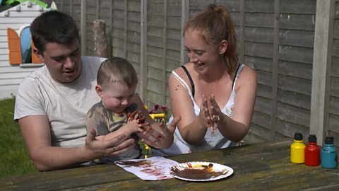 A family with their little boy are doing some finger painting in the garden.