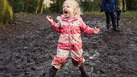 A little girl shouting as she splashes through the mud.