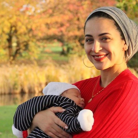 Mother with young baby held in her arms with trees and a pond in the background