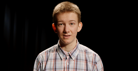 Caolan standing in front of a black background wearing a chequered shirt.