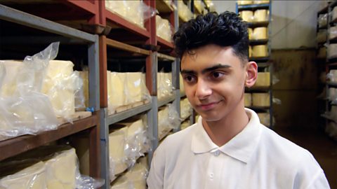 Bakr is discussing how the day went at the cheese farm. He's surrounded by huge blocks of cheese.