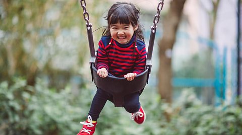 A girl smiling as she plays on a swing.