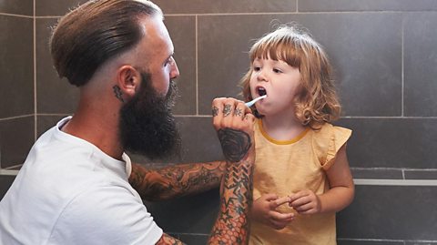 A dad brushing his little girl's teeth.