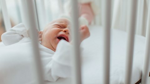 A crying baby in a cot.