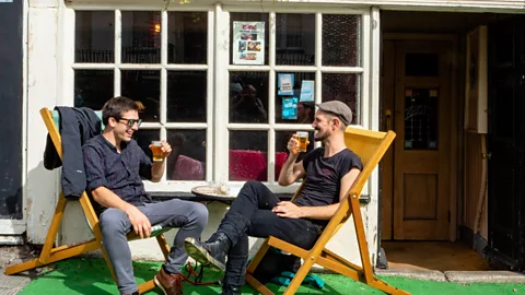 Alamy Two men sit in deckchairs outside a pub in Bristol, UK