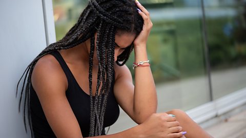 A teenage girl sat outside, leaning against a wall with her head in one hand