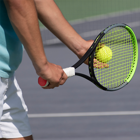 A person holding a racket prepares to serve a tennis ball