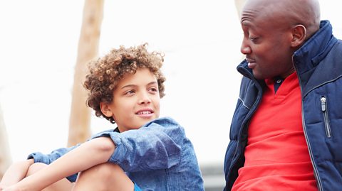 A young child is chatting to father outside. The adult man is looking at the young boy in surprise, whilst the child smiles.