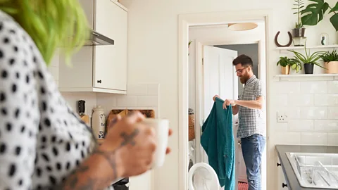 Getty Woman in the kitchen drinking coffee as man does the laundry