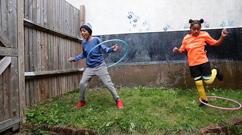 Two young children are playing on a small garden with hula hoops.