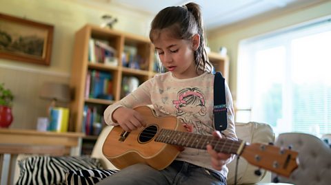 A young girl playing a ukulele