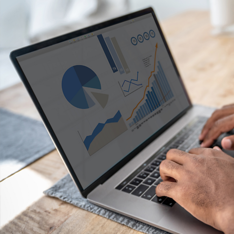 A person types on a laptop. The screen shows a variety of graphs and charts.