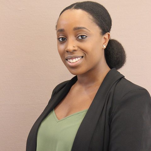 Young woman is smiling friendly at camera, wearing smart blazer jacket.