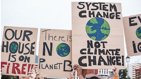 Protestors holding climate change placards saying System change not climate change, There is no planet B and Our house is on fire