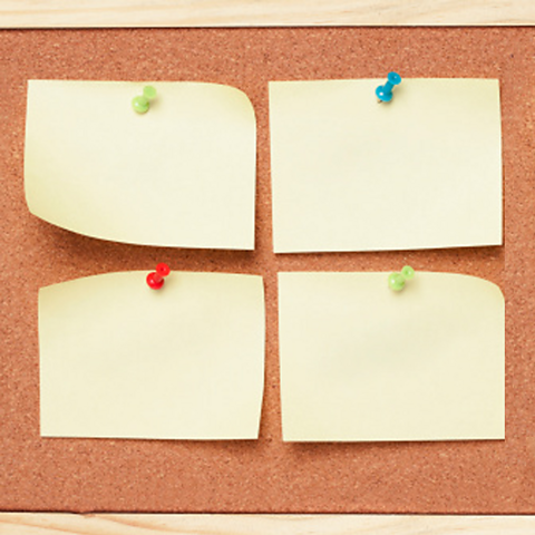 A photo of four pieces of yellow paper attached to a corkboard with different coloured pushpins.