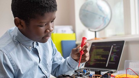 Male high school pupil building robot car in science lesson.