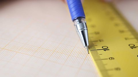 Close-up image of a pencil plotting a point on a graph, using a ruler.