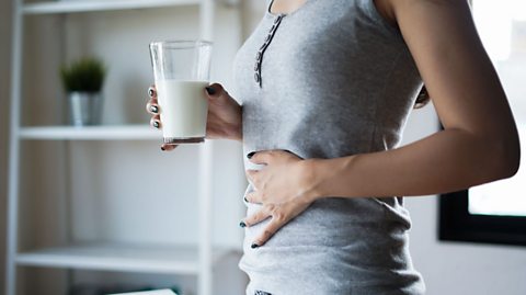 Woman with a glass of milk holding her stomach