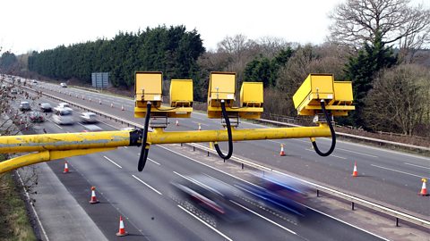 Three yellow speed cameras above a motorway with traffic flowing beneath