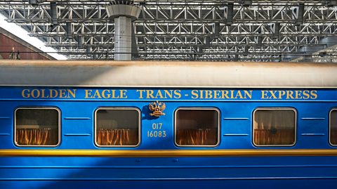 A photo of a bright blue carriage on The Golden Eagle Trans Siberian Express Train, with the name written in gold on the side